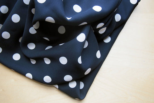Black silk georgette with large white polka dots folded to show fabric drape and texture on a wood surface