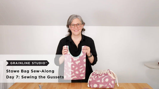 Woman holding up a finished Stowe Bag in mauve printed canvas with teal binding beside a second completed bag on the table
