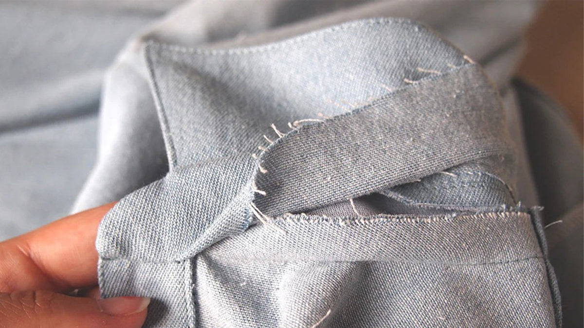 Hand holding assembled Alder collar and collar stand on gray denim showing interfaced layers and graded seam allowances