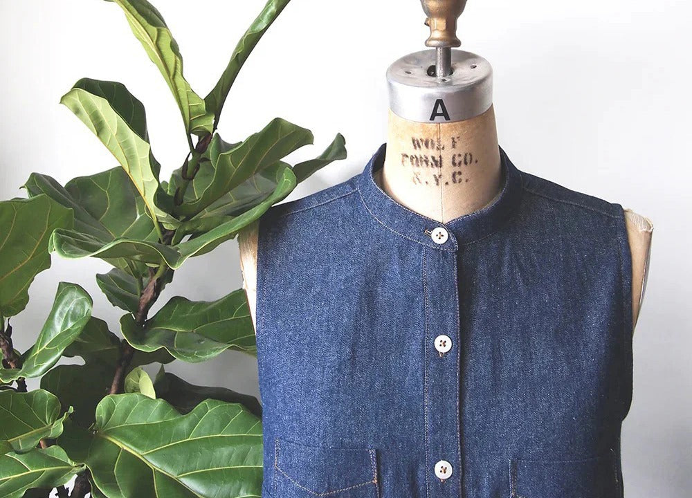 Alder shirtdress on dress form in dark denim showing band collar variation with white buttons and fiddle leaf fig plant