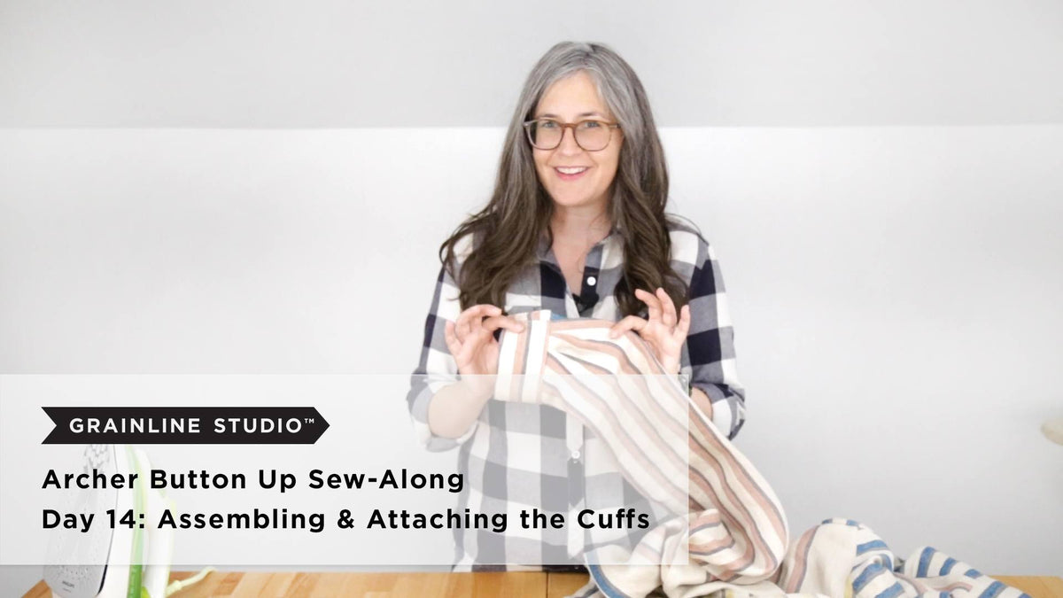 Woman smiling and holding up the end of a striped linen Archer sleeve to show the attached cuff.