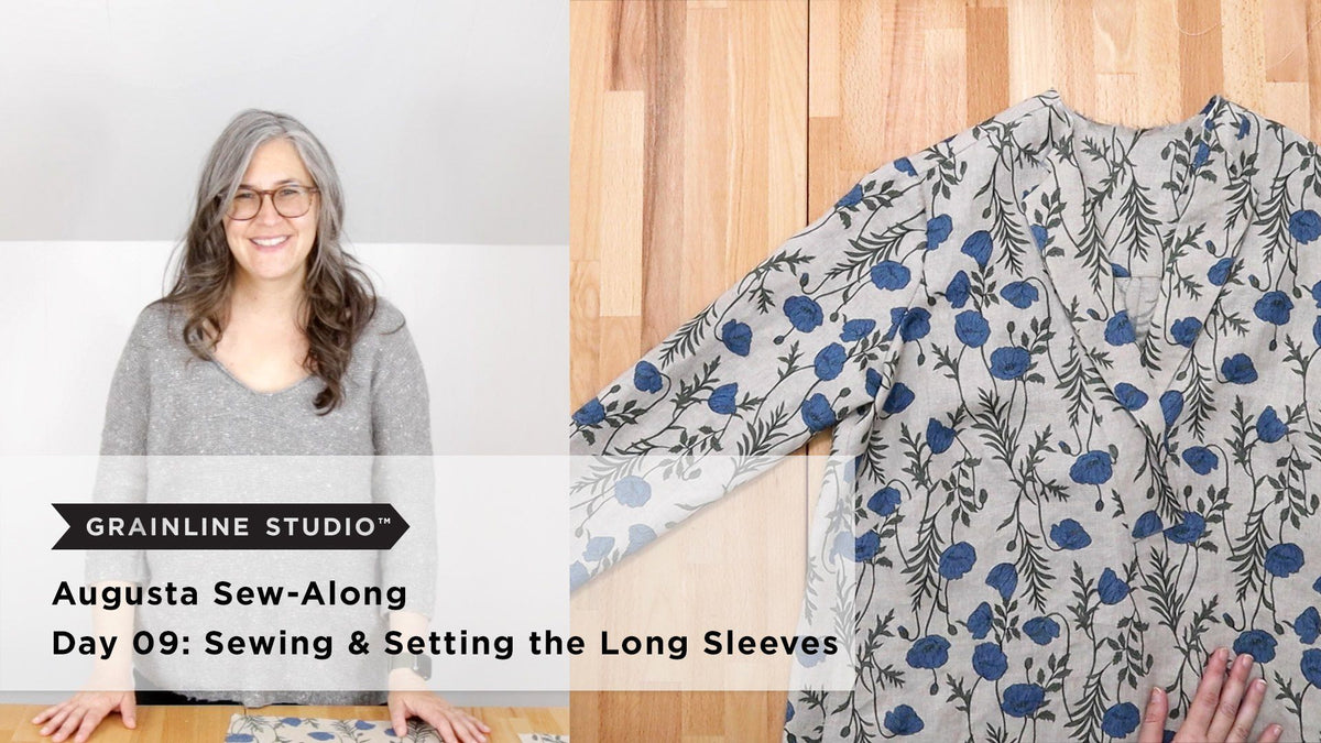 Woman smiling in a gray sweater beside a blue poppy print Augusta with long sleeves laid flat on a wood table