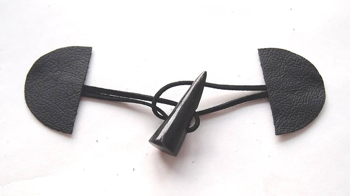 Completed toggle closure with black leather tabs connected by black cord threaded through black toggle button on white surface