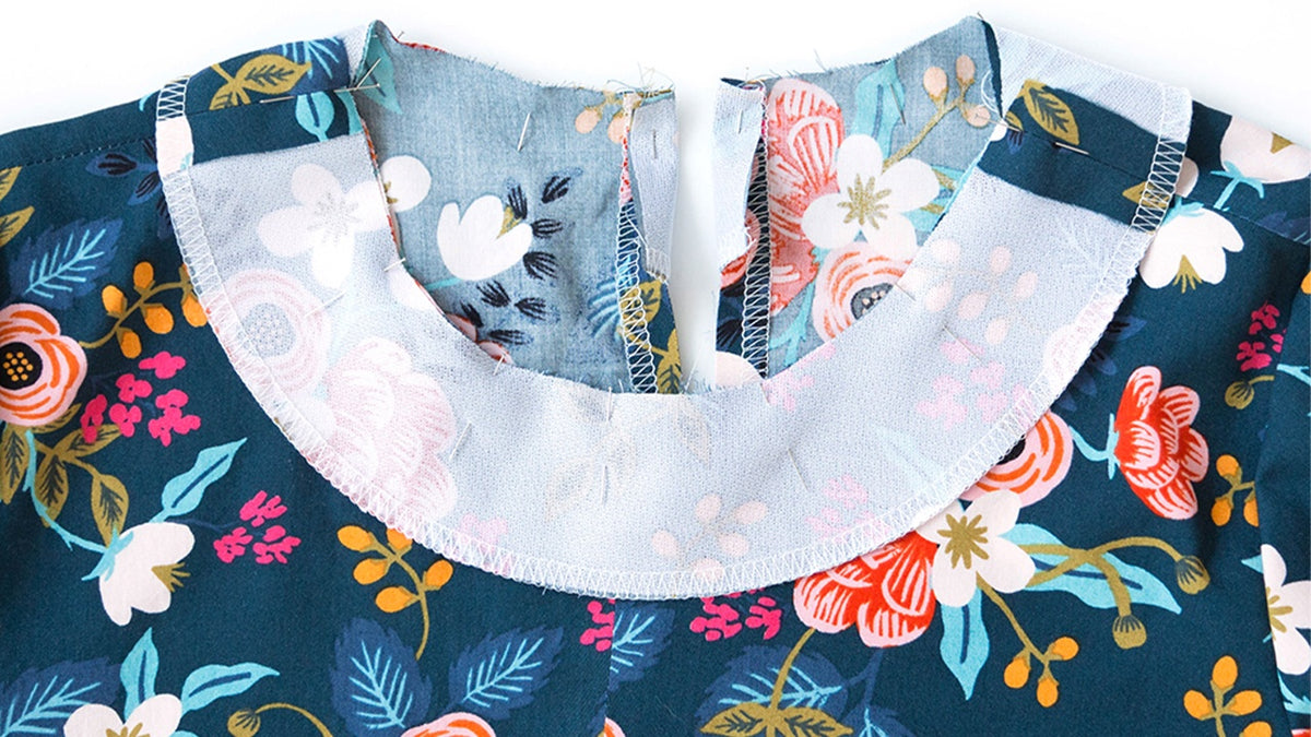 Neckline facing pinned to Farrow Dress neckline showing proper alignment at center back opening on navy and light blue floral fabrics.