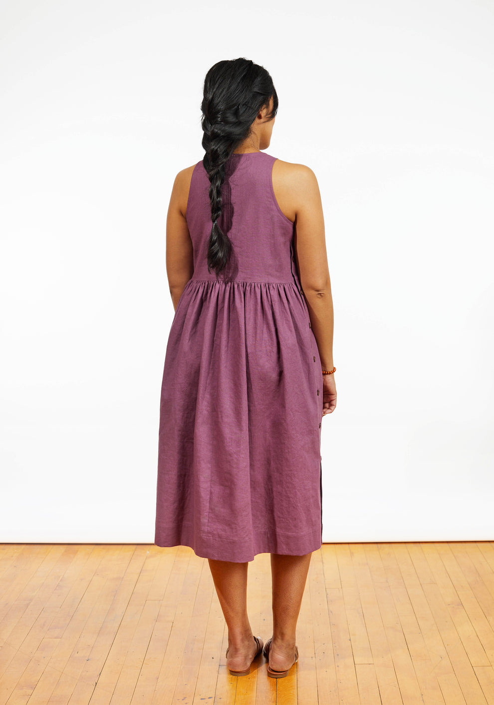 Back view of Austin Dress in mauve linen showing gathered skirt and sleeveless bodice, worn by model.