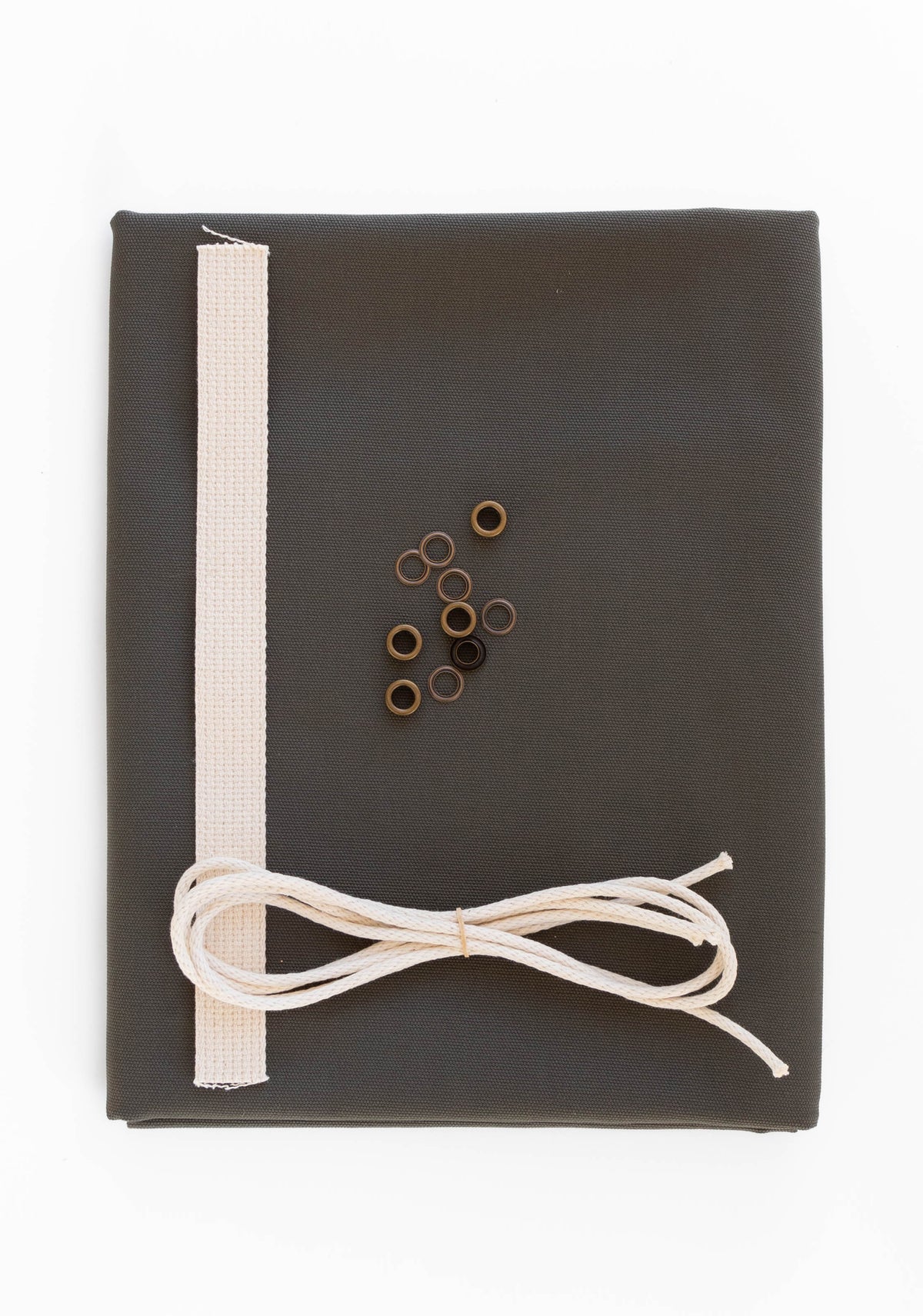 Flatlay of Field Bag kit in pewter green canvas with cotton web strap, cotton cord, and antique brass grommets.