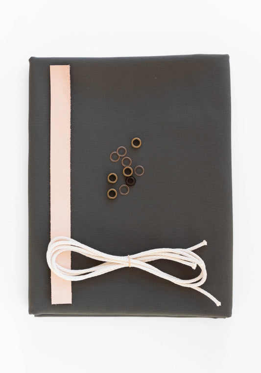 Flatlay of Field Bag kit in pewter green canvas with leather strap, cotton cord, and antique brass grommets.