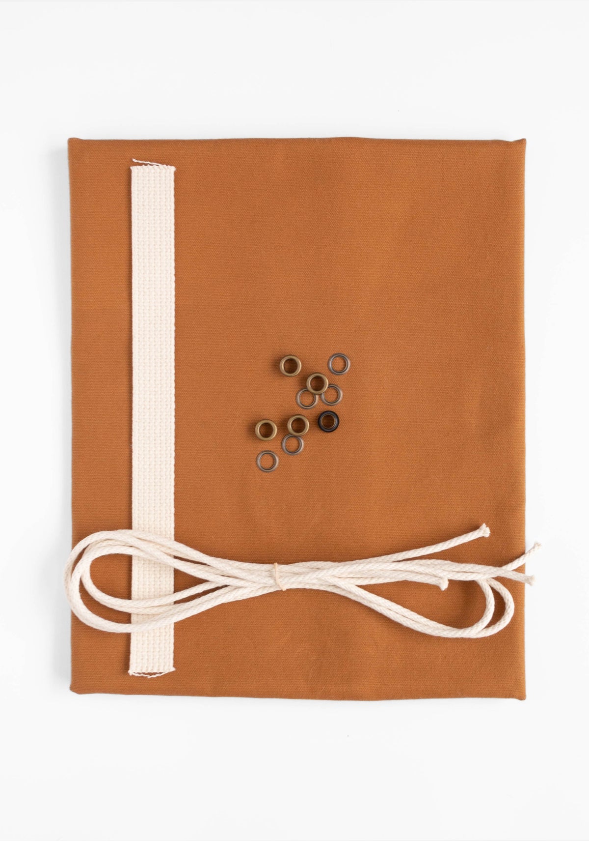 Flatlay of Field Bag kit in toffee canvas with cotton webbing, cotton cord, and antique brass grommets.