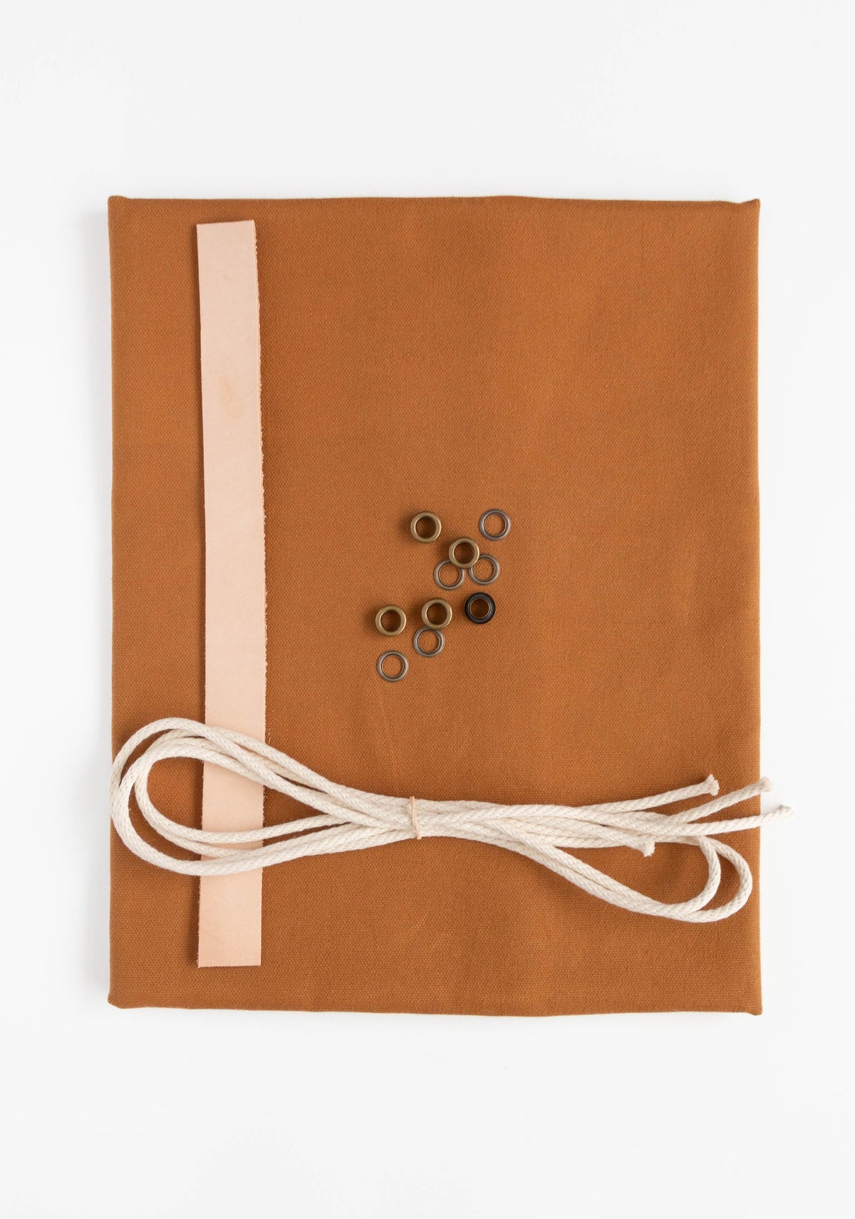 Flatlay of Field Bag fabric kit in toffee canvas with leather strap, cotton cord, and antique brass grommets.