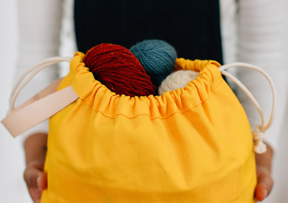 Yellow canvas Field Bag with drawstring closure holding colorful yarn skeins in red, teal, and cream