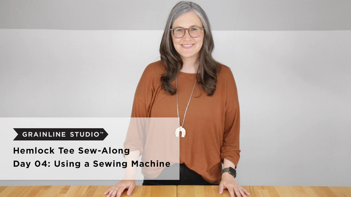 Hemlock Tee Sew-Along Day 04 thumbnail, woman standing at wood table for sewing machine lesson