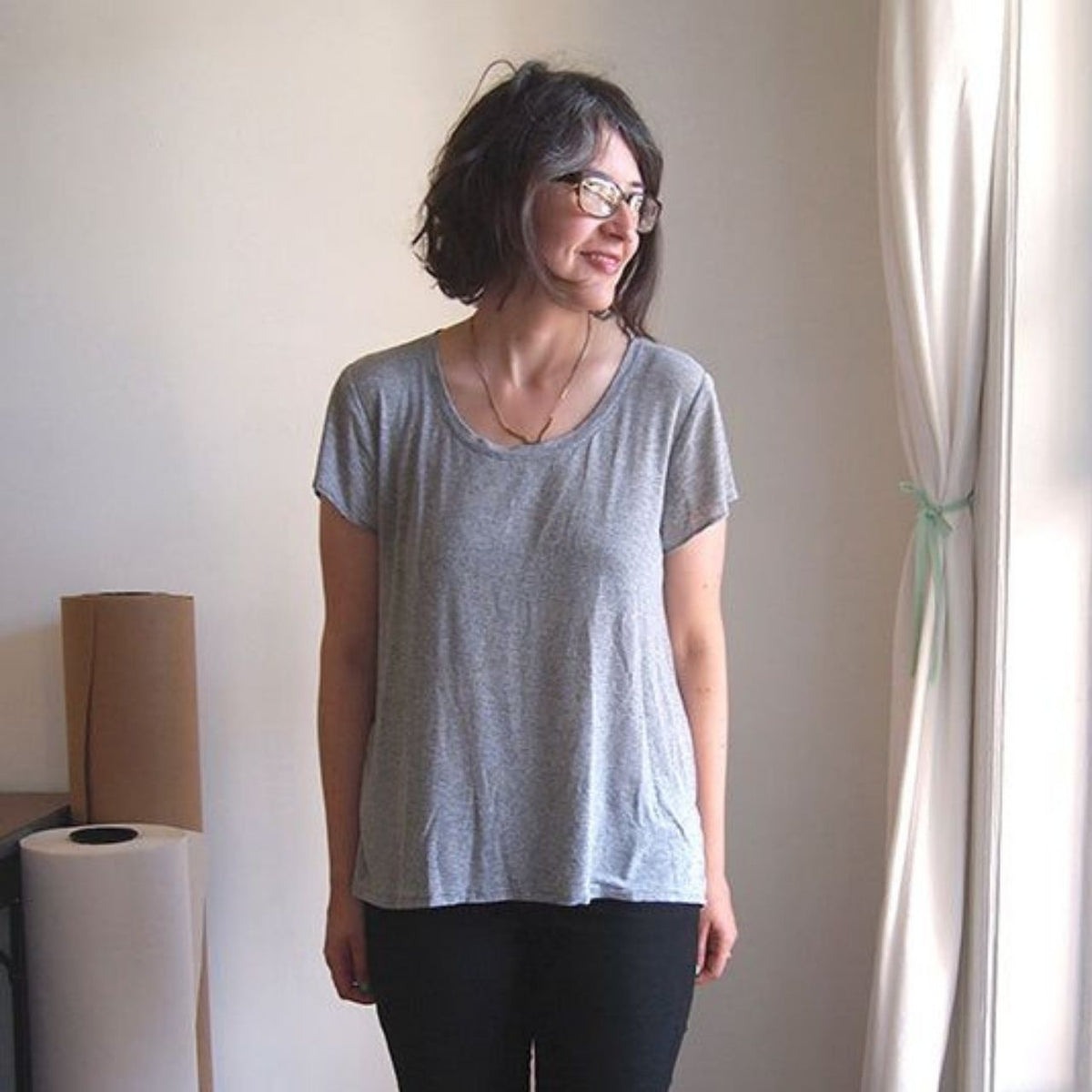 Woman wearing a Scout Tee sewn in heathered gray knit fabric with a scoop neckline and cap sleeves, styled with black pants.
