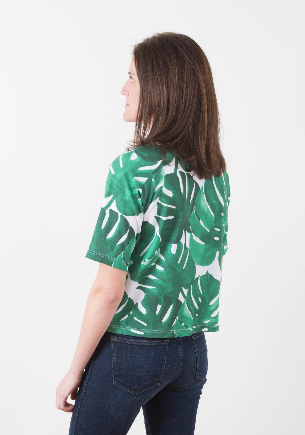 Back view of a woman wearing a short-sleeve Linden Sweatshirt with a green monstera leaf print.