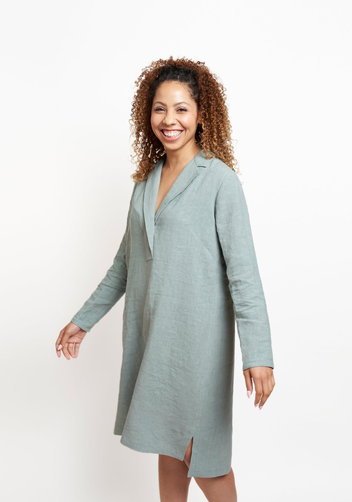 Side view of blue-green Augusta Dress in motion, showing long sleeves and side slit above the knee.