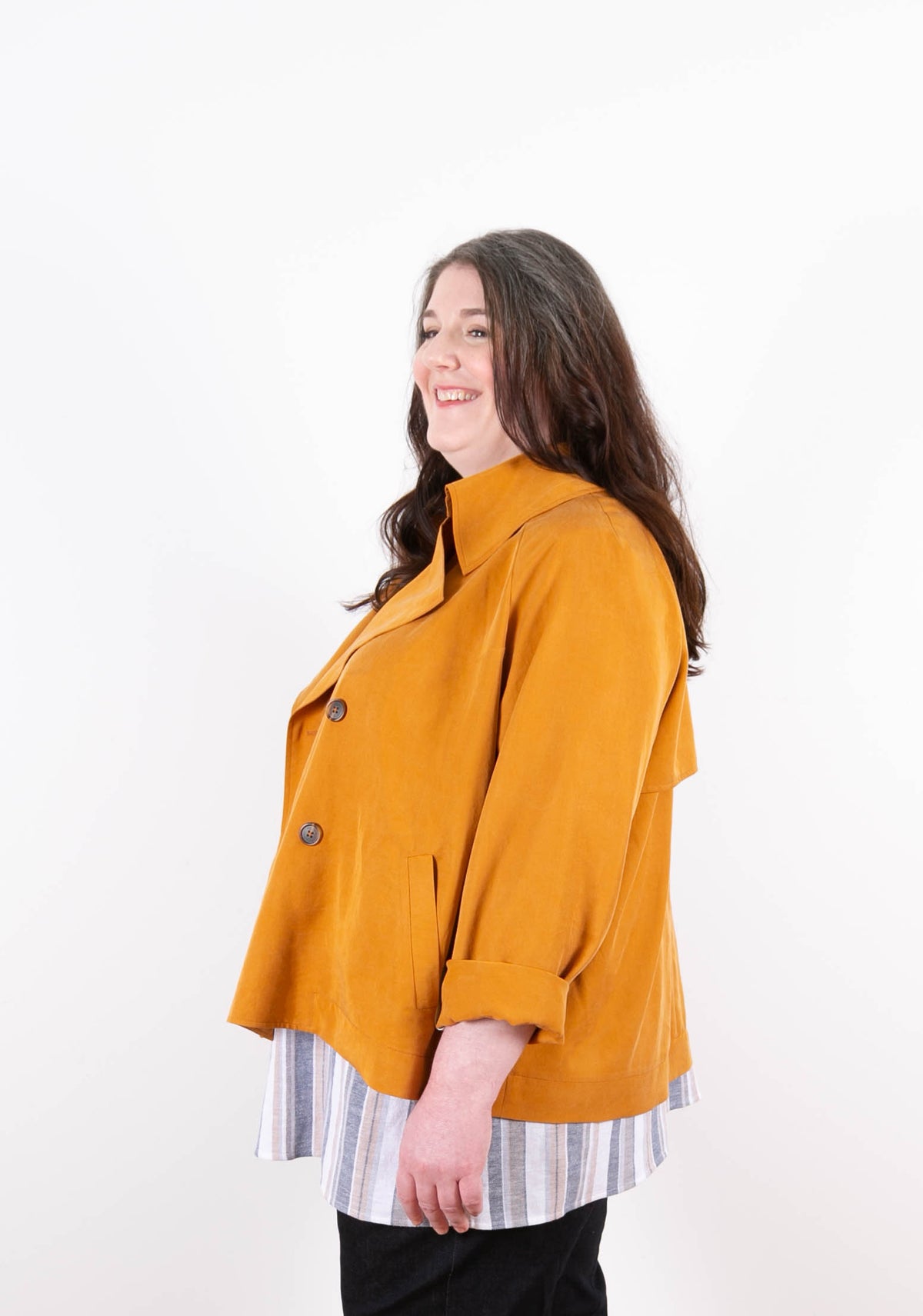 Model in golden Cortland Trench from the side, layered over striped shirt.