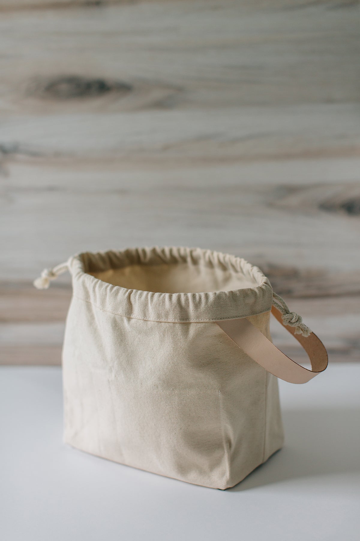 Natural canvas field bag empty and open, showing leather handle and drawstring closure.