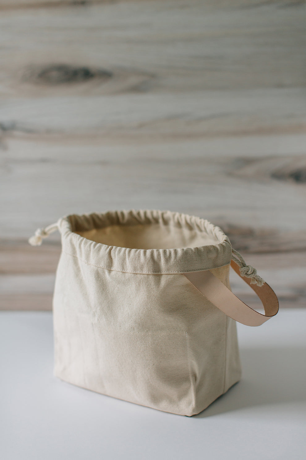 Natural canvas field bag empty and open, showing leather handle and drawstring closure.