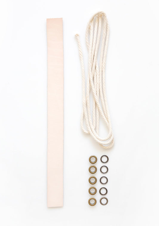 Model: Leather Handle | Flatlay of Field Bag notions kit with natural leather strap, drawstring cord, and brass grommets.