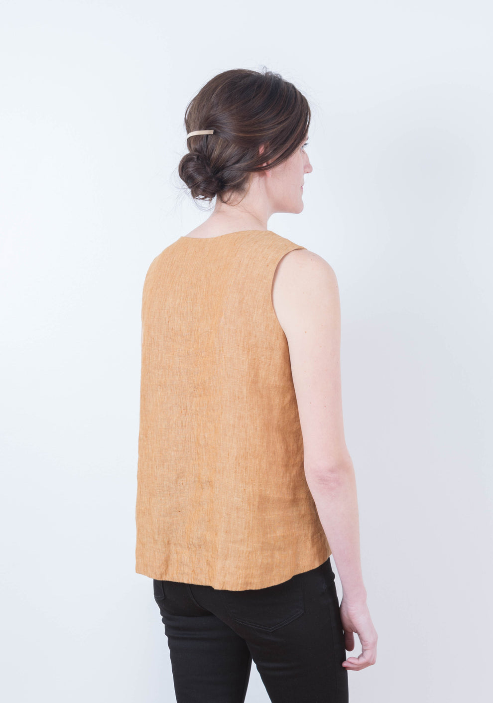 Back view of sleeveless Hadley Top in rust linen with curved hem, worn by model.