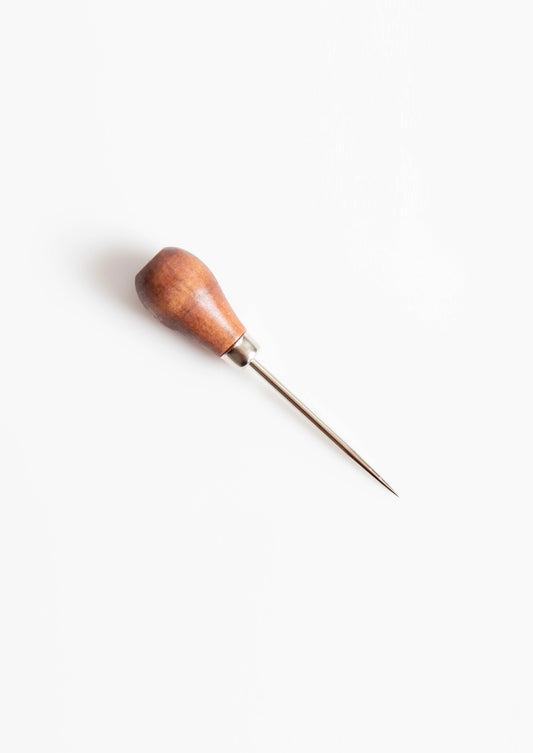 Flatlay of a single awl with a wood handle and sharp metal point on white background.