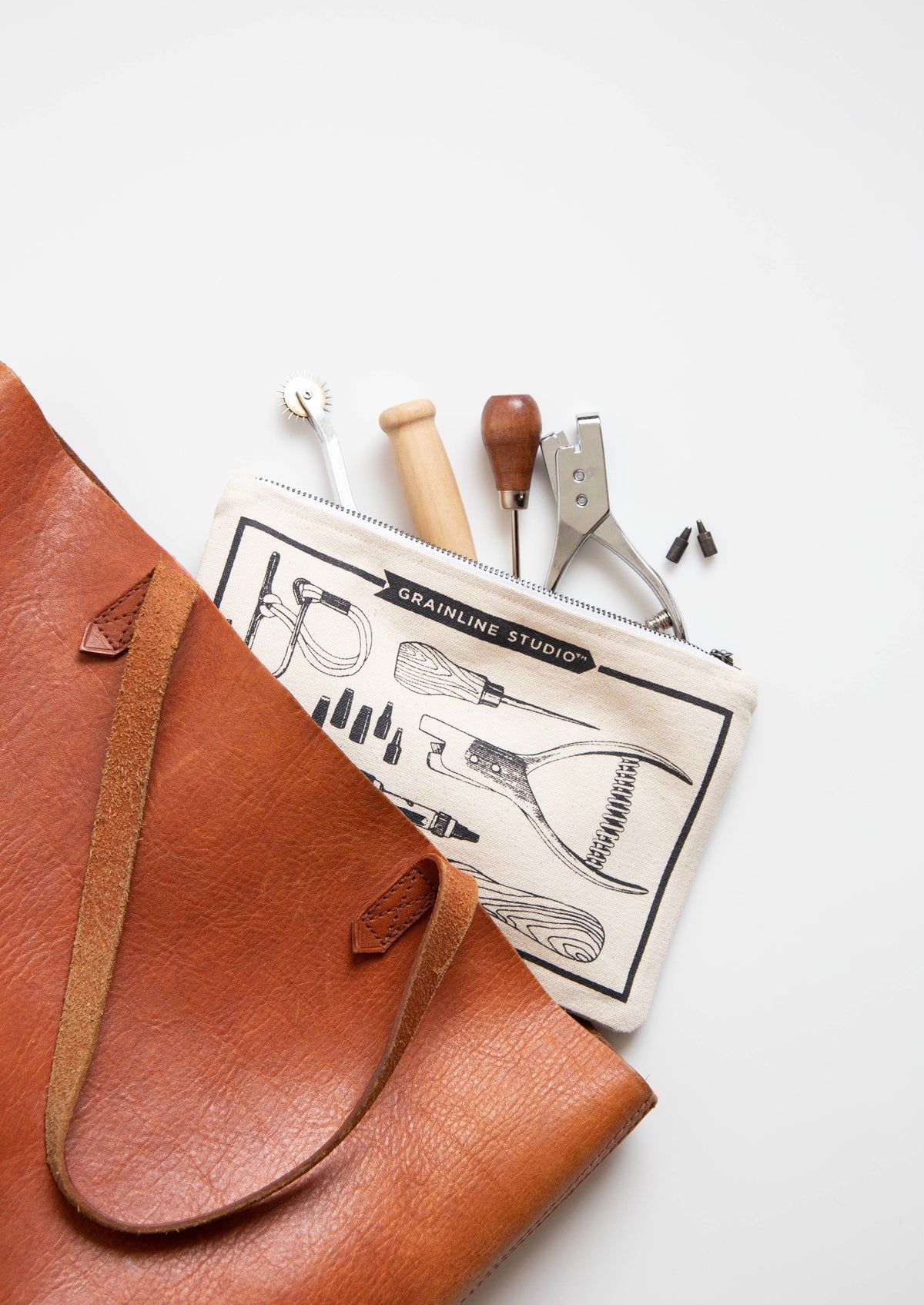 Grainline Studio Pattern Tools pouch with tools partially tucked into a leather bag on white background.