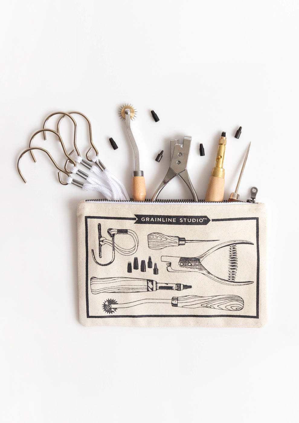 Flatlay of Grainline Studio Pattern Tools pouch with sewing tools and hardware spilling out on white background.