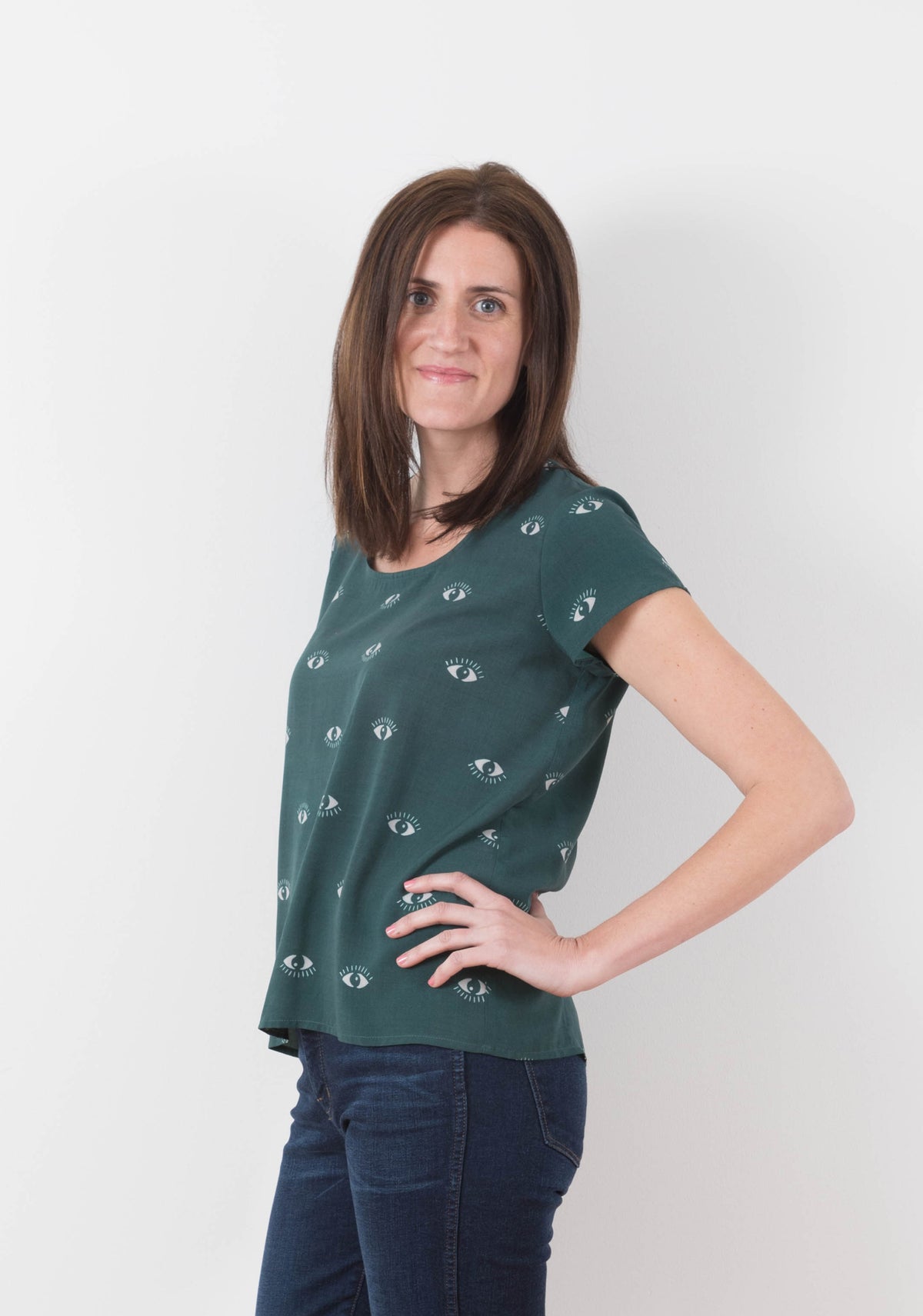 Model wearing green Scout Tee with eye print in side view, hand on hip.