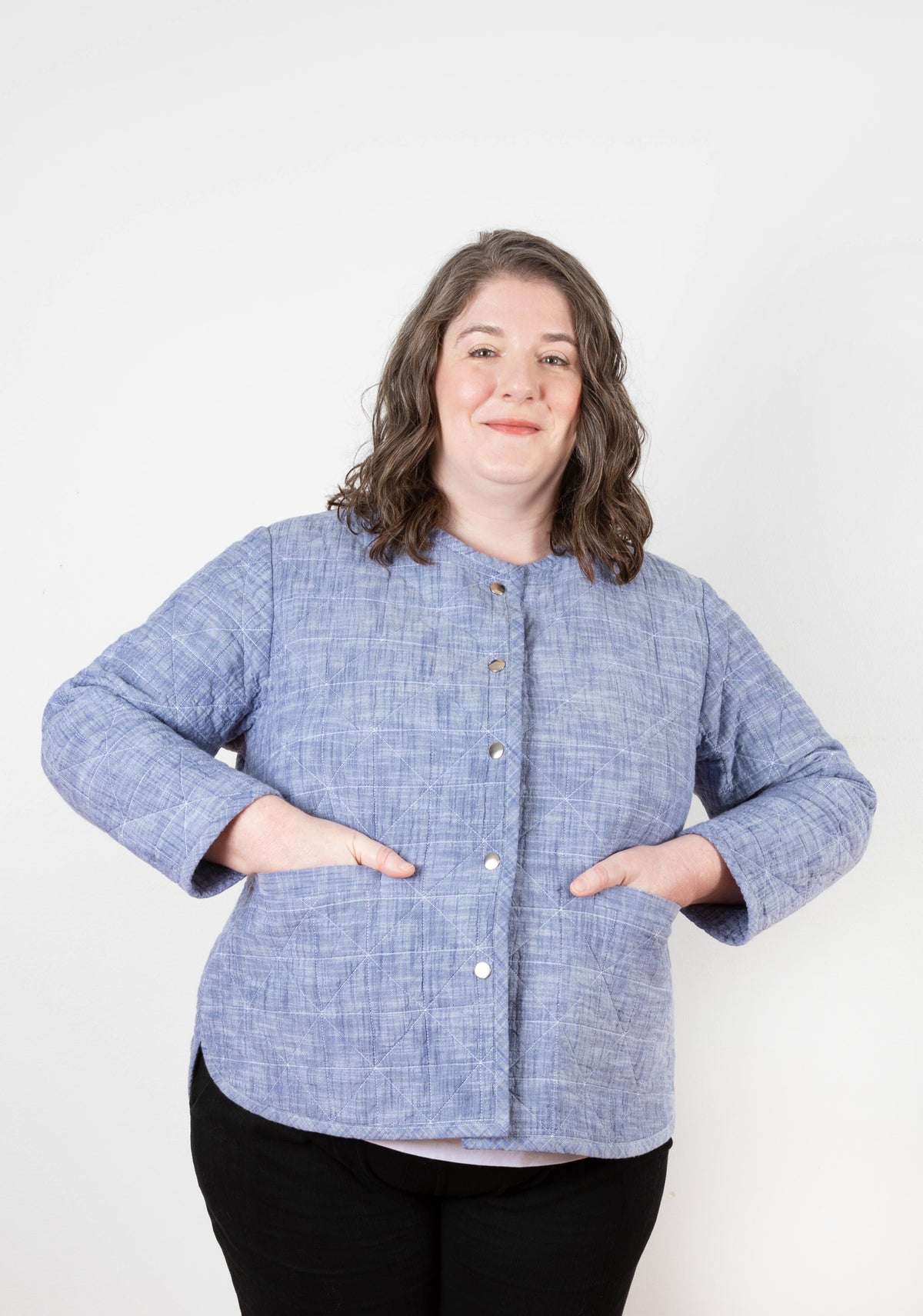 Model wearing Tamarack Jacket in blue chambray with front snaps and hands in pockets, facing forward.