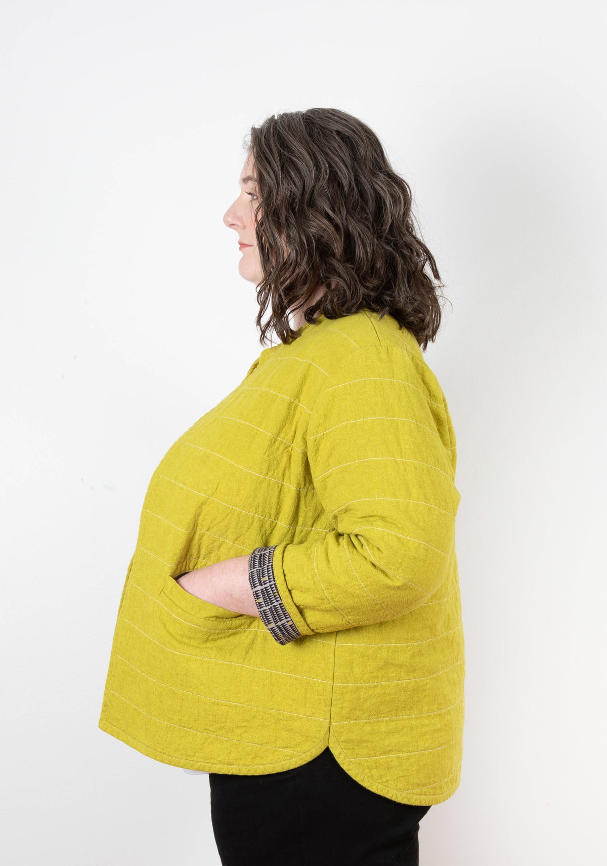 Left profile of model wearing mustard yellow Tamarack Jacket with welt pocket and horizontal quilting.