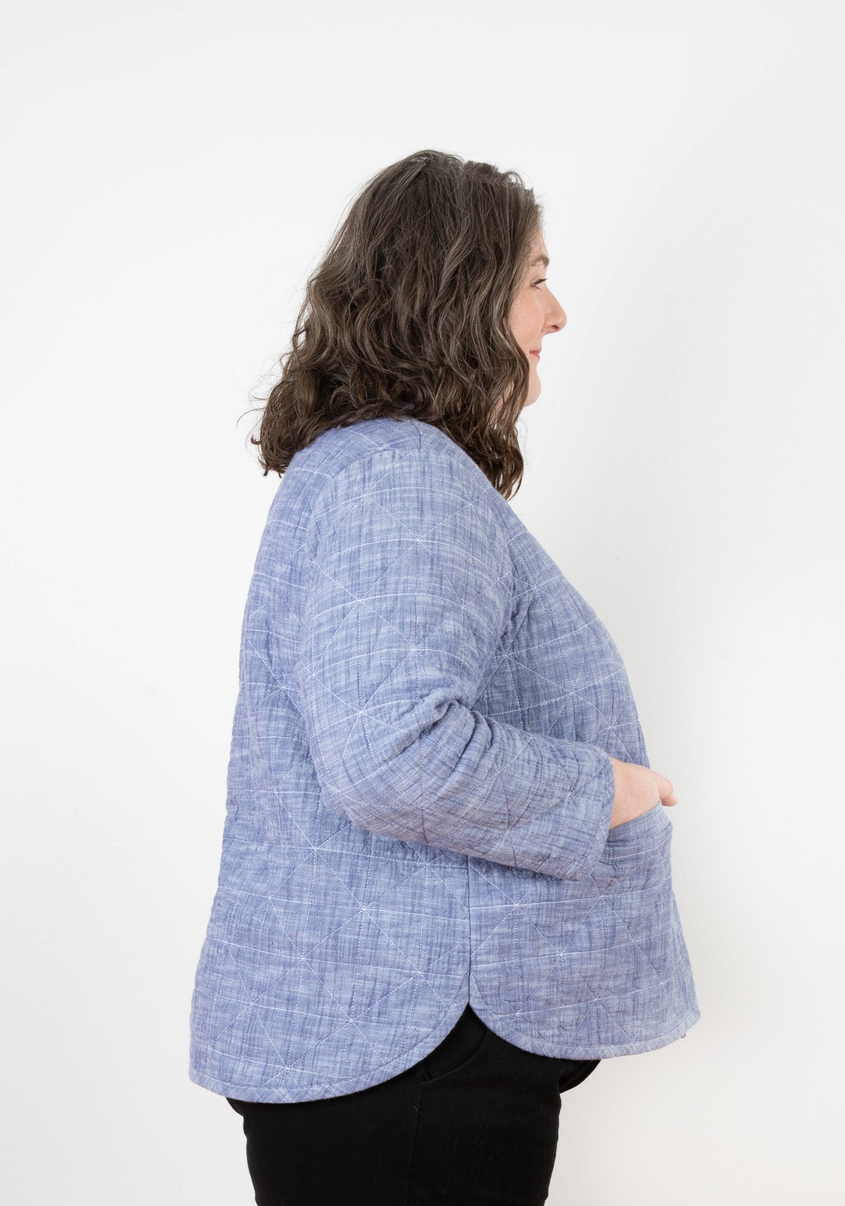 Left profile of model in blue chambray Tamarack Jacket with diamond quilting and curved hem.