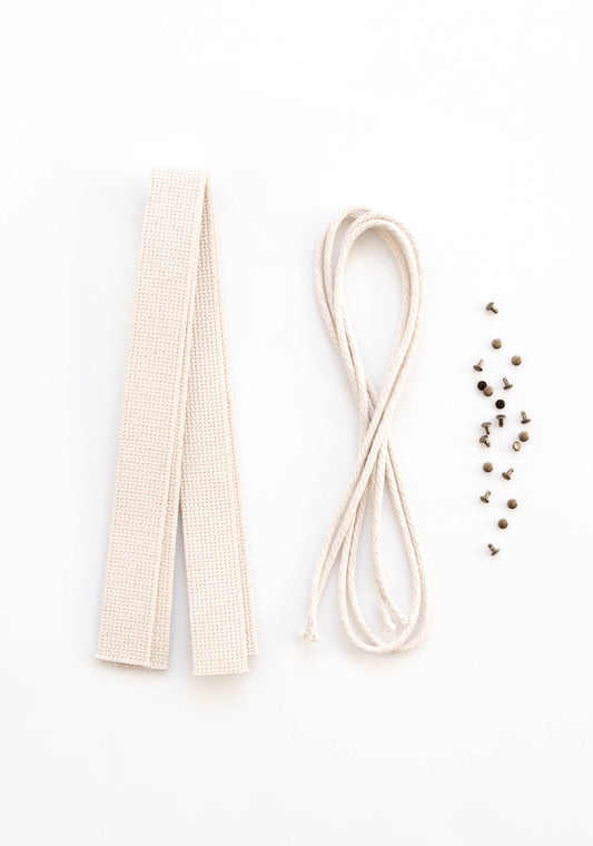 Flatlay of Town Bag Notions Kit showing cotton webbing handles, drawstring cord, and antique brass rivets on white background.