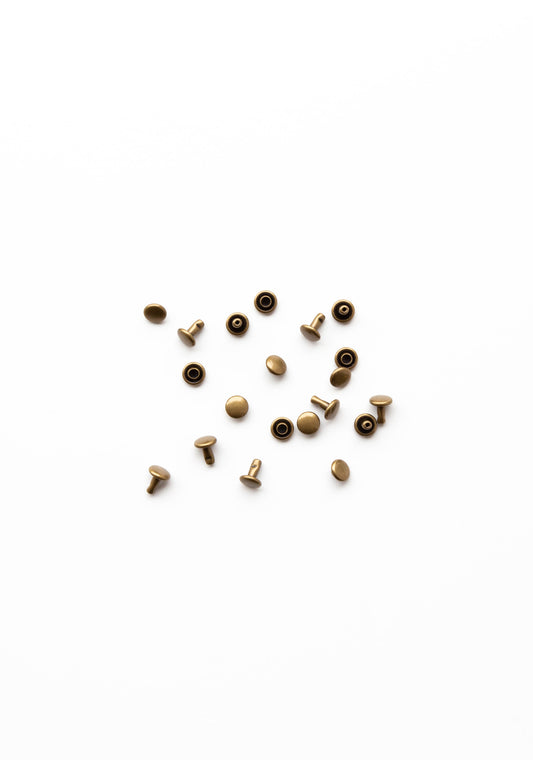 Flatlay of antique brass rivets for the Town Bag sewing pattern on a clean white background.