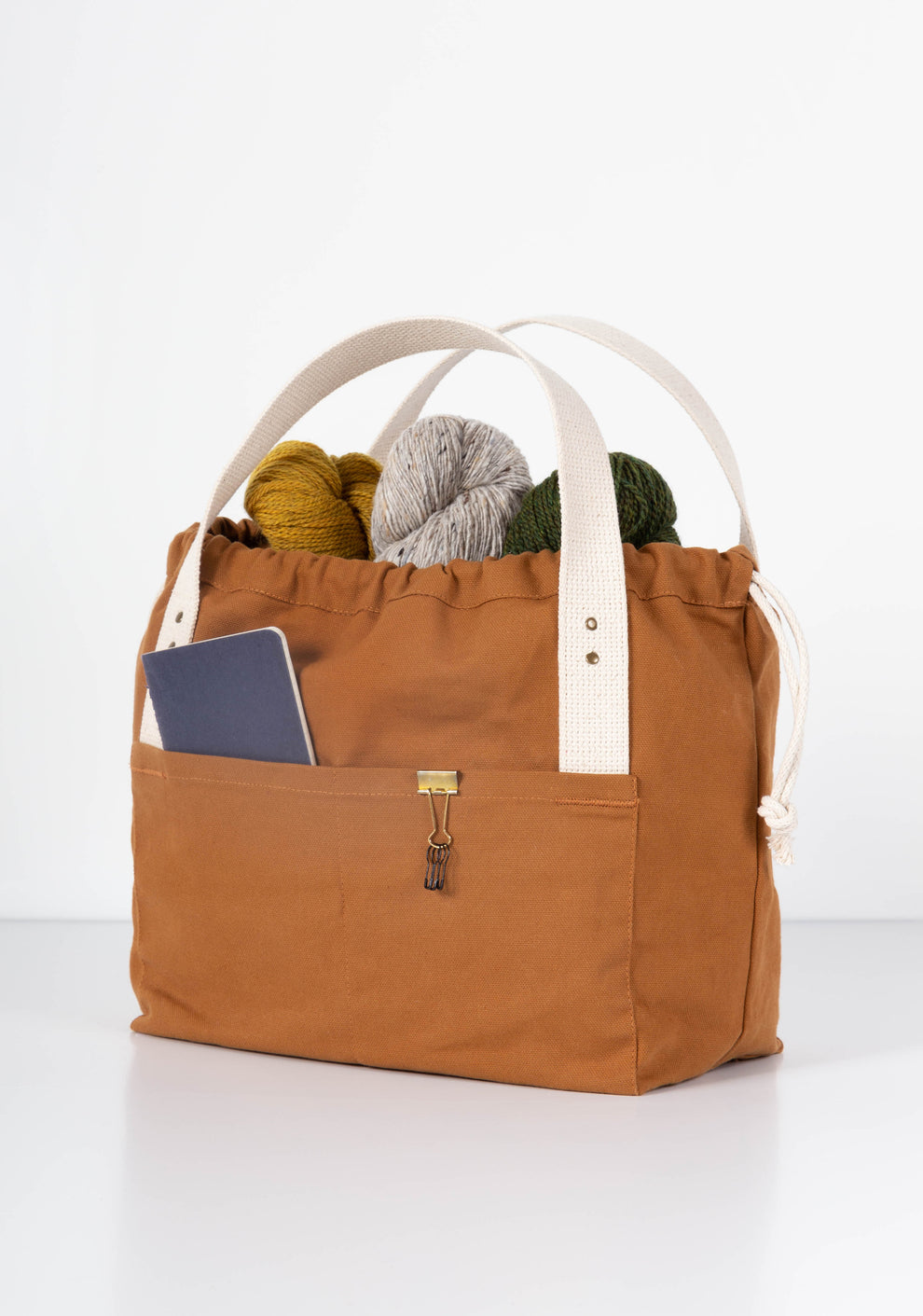 Angled view of brown Town Bag filled with yarn and notebook in outer pocket.