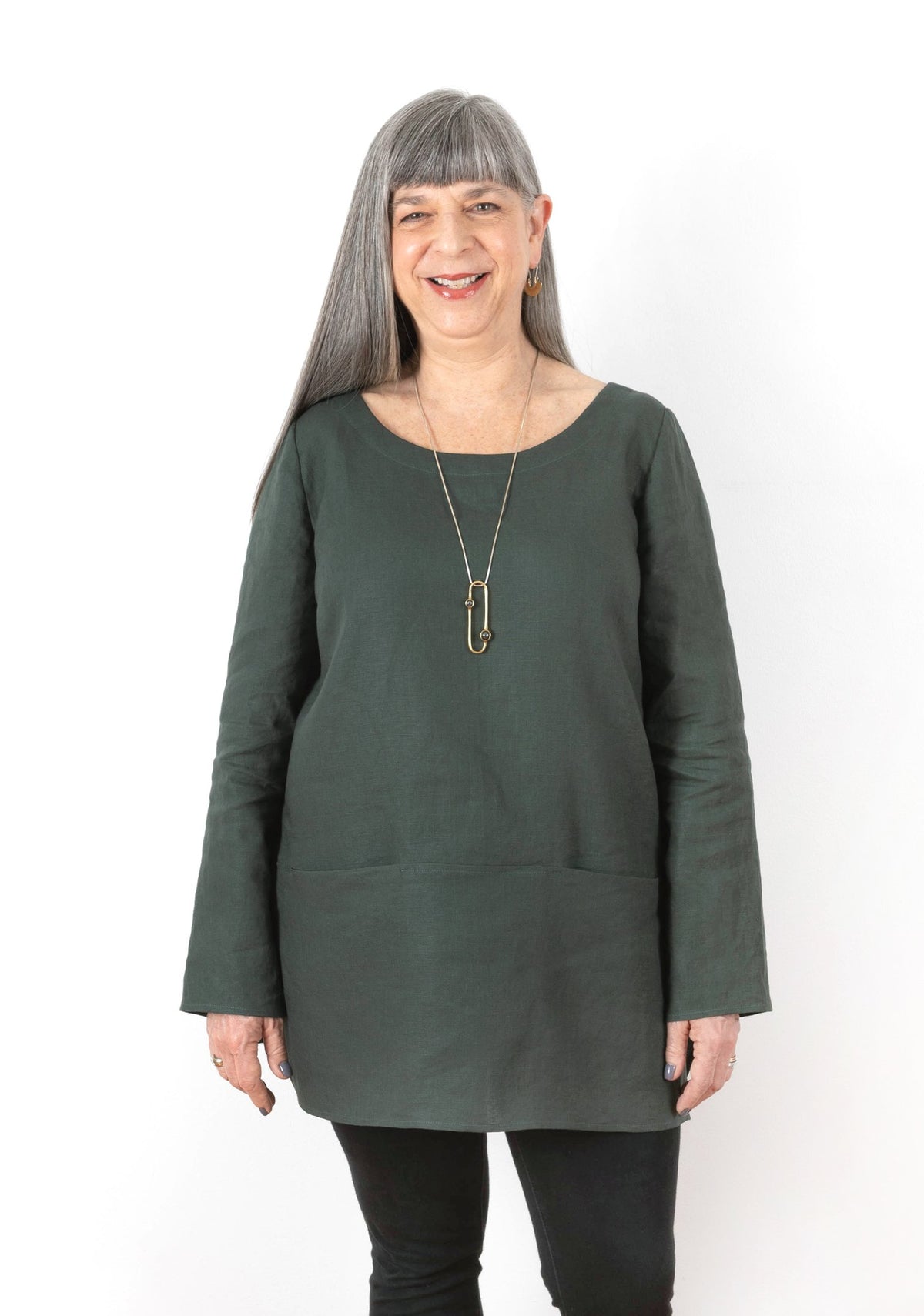 Front view of Uniform Tunic with long sleeves and inseam pockets, in dark green linen, modeled standing straight.