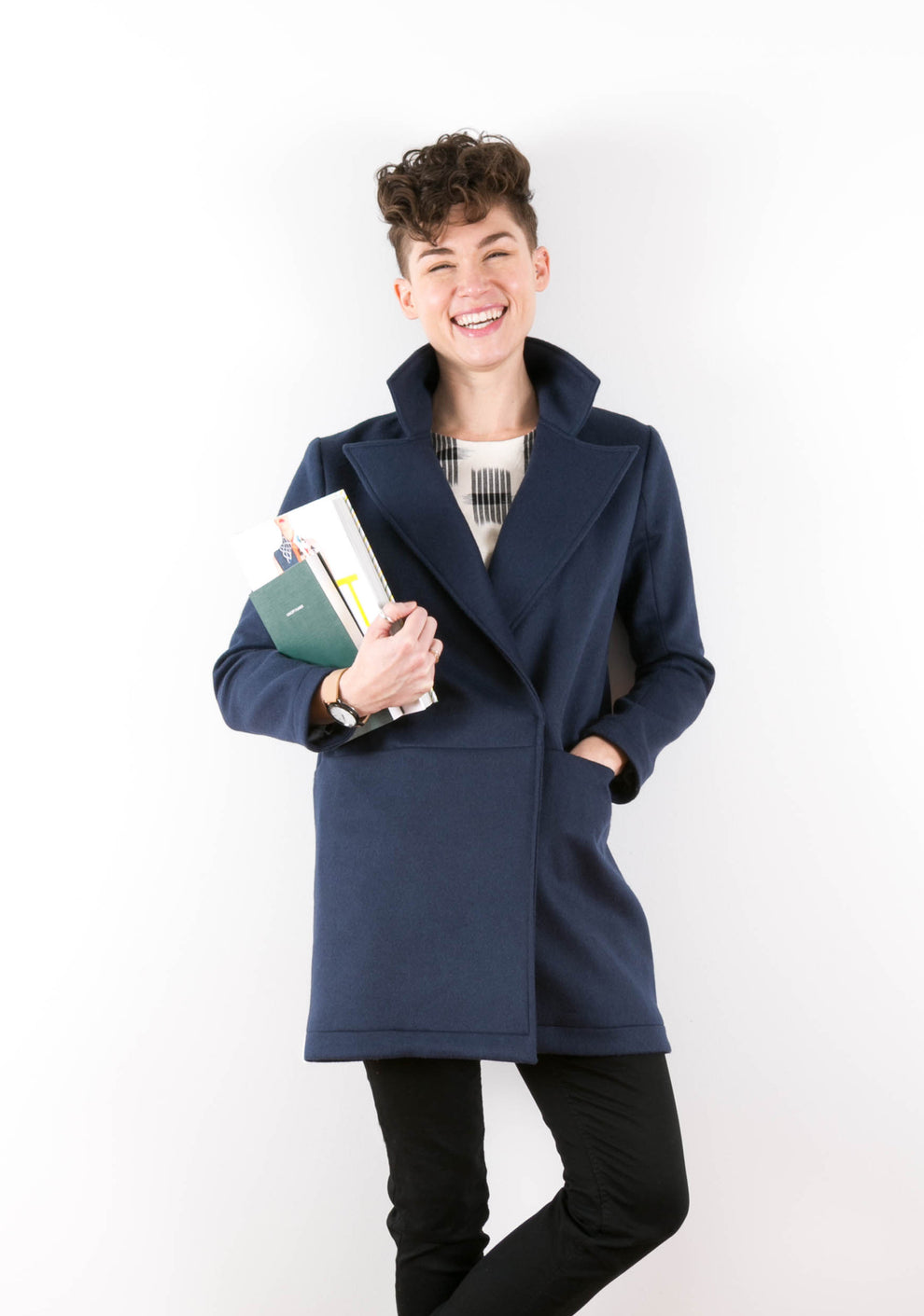 Model laughing while wearing navy Yates Coat with collar popped, holding books in left arm.